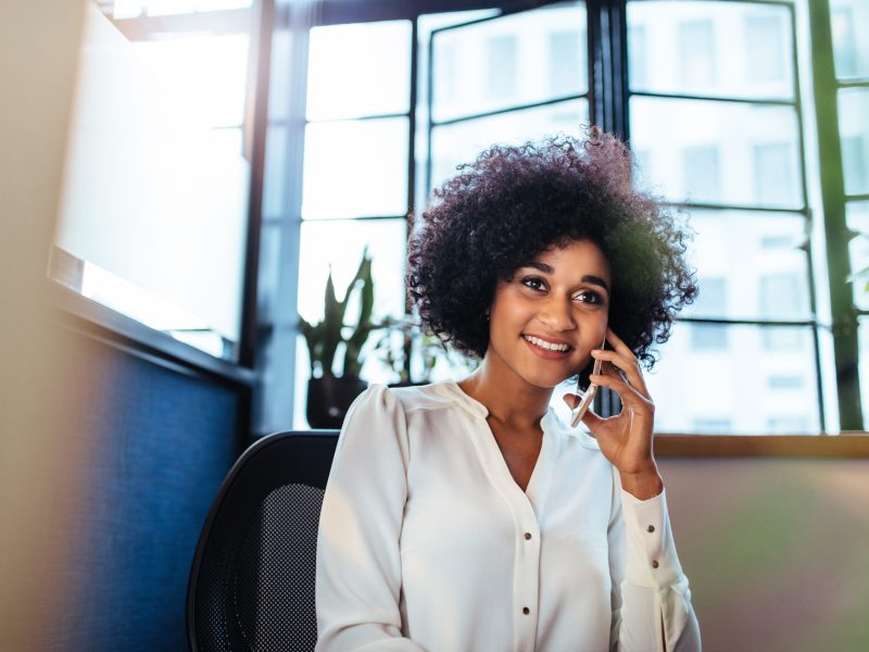 Indoor shot of beautiful african businesswoman using smart phone in office. Female executive making a phone call.